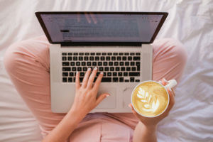 Person using laptop on bed with coffee