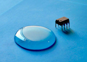 Tiny semiconductor chip on blue surface next to drop of water